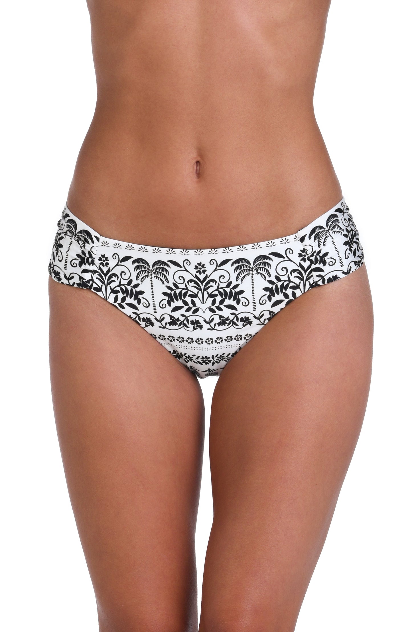 Model is wearing a white and black monochromatic patterned side shirred hipster bottom that features an allover tropical motif with hints of palm trees and pineapples set against a black background.